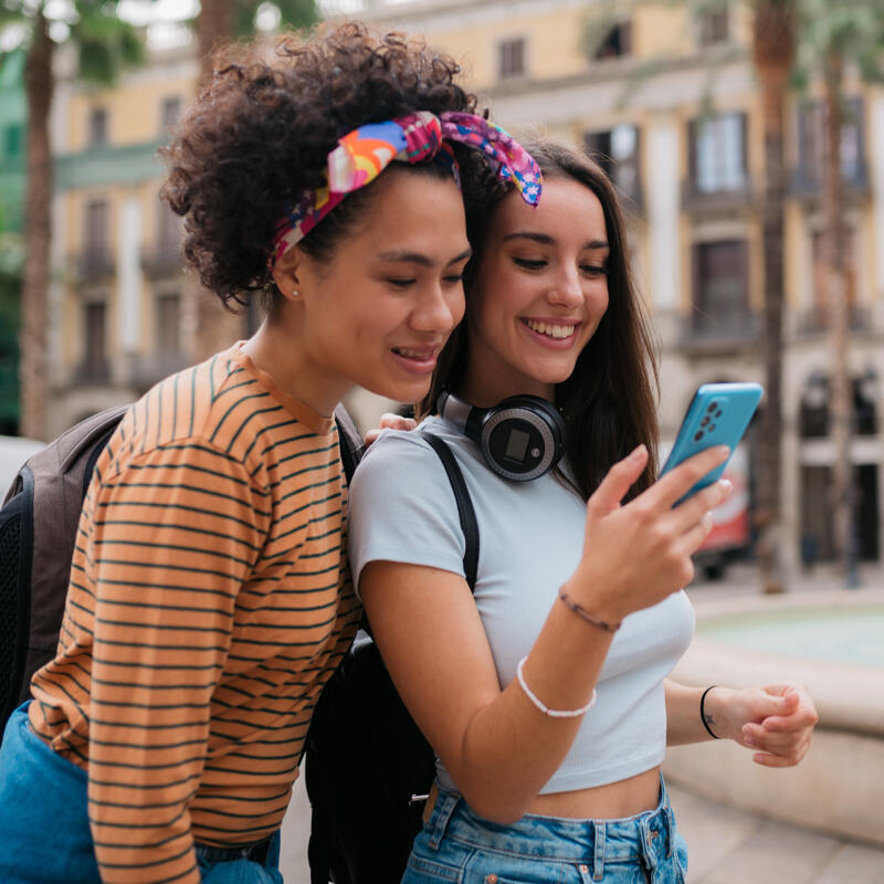 Young diverse female romantic couple enjoying their vacation in Barcelona, using a smart phone and smiling
