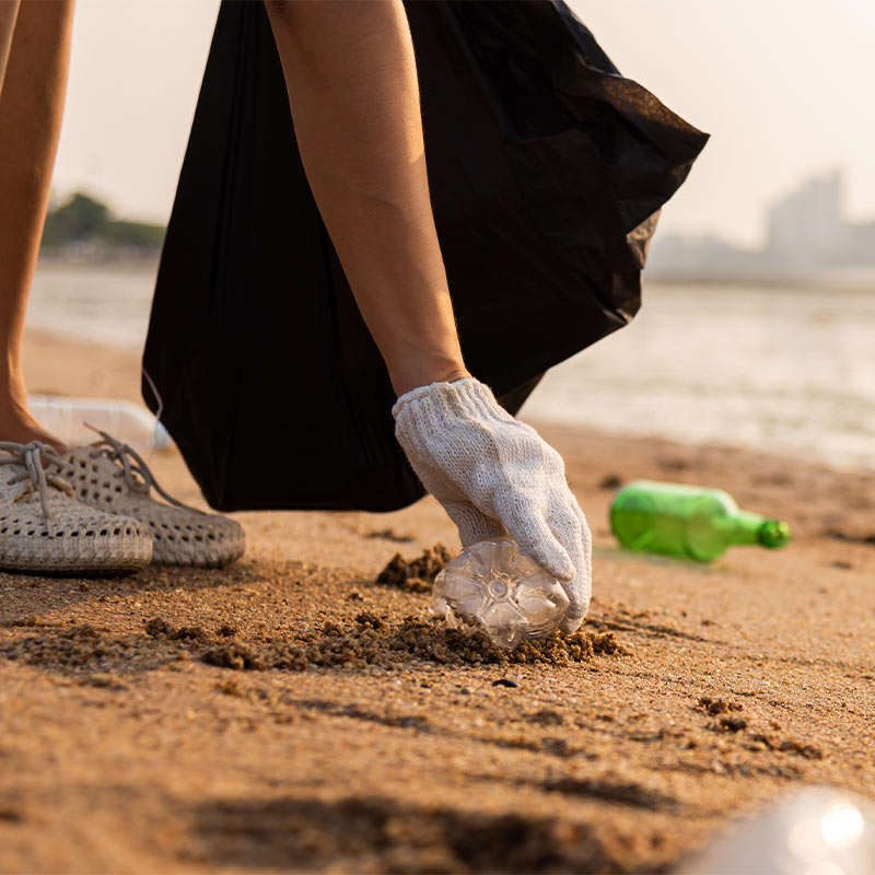 Close-up of a hand with a protective glove picking up debris on the beach
