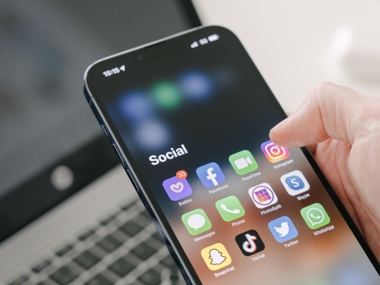 Gothenburg, Sweden - March 23, 2022: A man's hand holds a Iphone 13 Pro max with social media apps, against the background of a laptop. Blurred background. Selective focus.